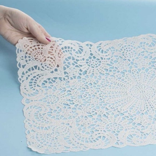 A hand holds a lace vinyl placemat, highlighting the laser-cut lace patterns.