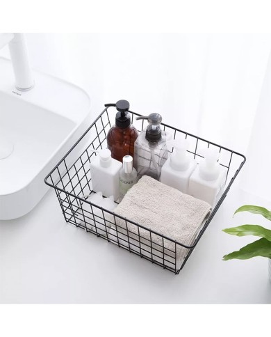 Black wire basket filled with various toiletries, a towel, and a plant in the background. Black wire basket filled with various toiletries, a towel, and a plant in the background.