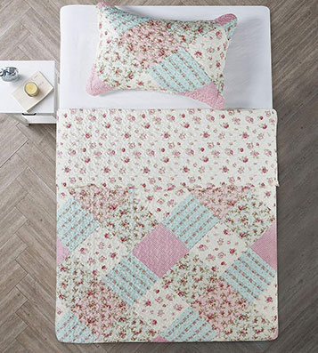 A bed with a charming single quilt and matching pillowcase featuring a mix of floral and pastel designs in pink, blue, and cream.