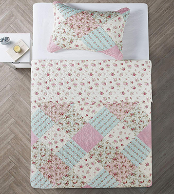 A bed with a charming single quilt and matching pillowcase featuring a mix of floral and pastel designs in pink, blue, and cream