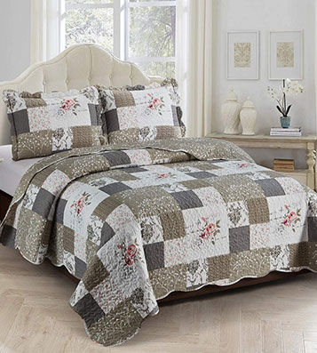 A cozy bedroom featuring a khaki brown and beige patchwork quilt with a vintage rose design.